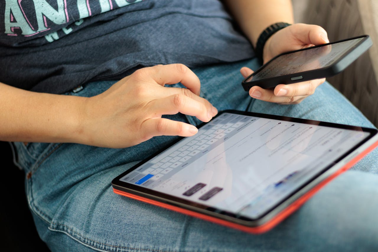 Close-up of adult using a tablet and smartphone indoors, showcasing digital connectivity and multitasking.