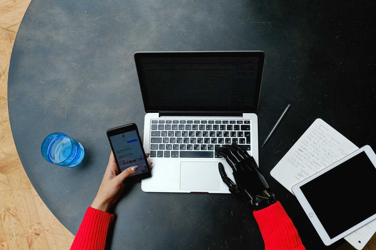 A person using a laptop, smartphone, and tablet with a prosthetic hand, emphasizing digital connectivity.